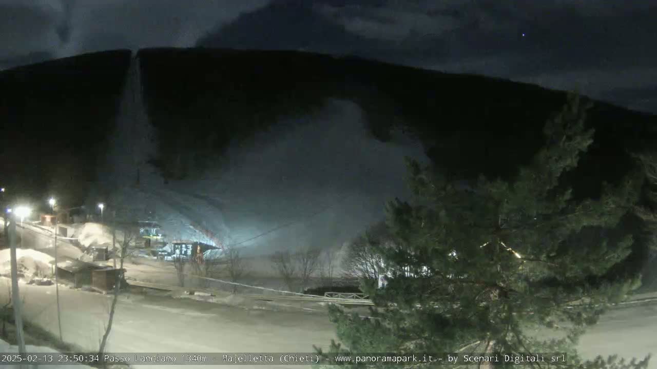 A nighttime view of a snowy mountainside with a structure at its base, under a dark, cloudy sky.