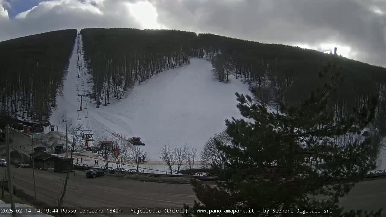 A ski slope with a chairlift is partially covered in snow under a cloudy sky.