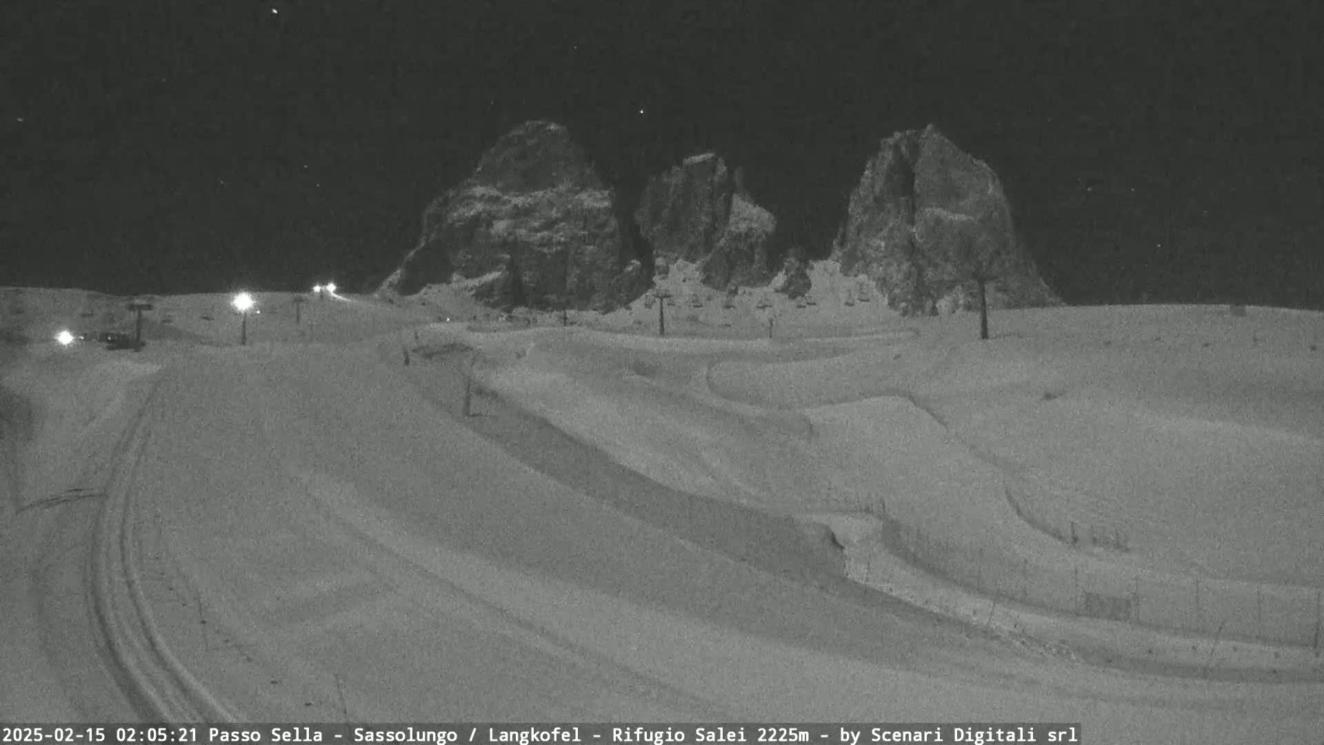 A nighttime, snow-covered ski slope with several ski lifts and rock formations in the background under a clear, starry sky.