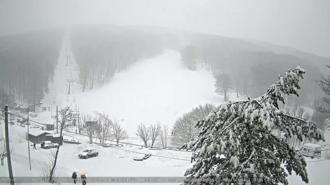 A snow-covered ski slope with a chairlift and several cars parked in the surrounding snowy area during a heavy snowstorm.