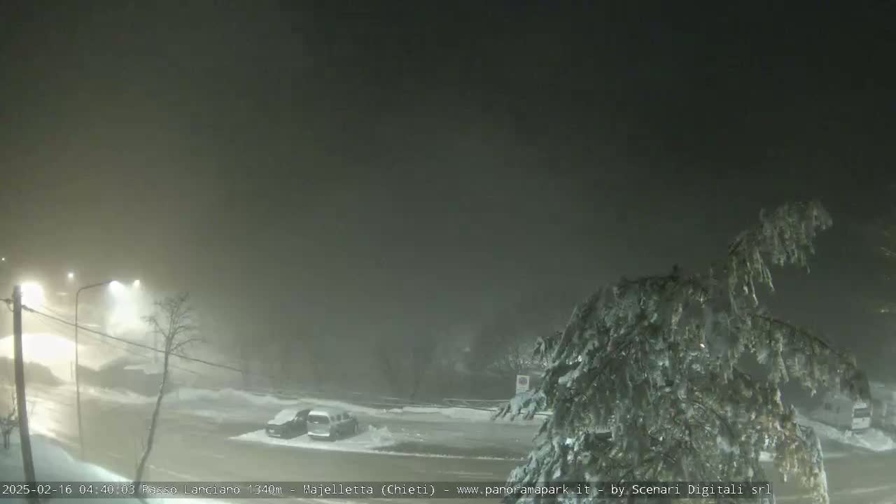 A snow-covered parking lot and road are dimly lit under a foggy night sky.