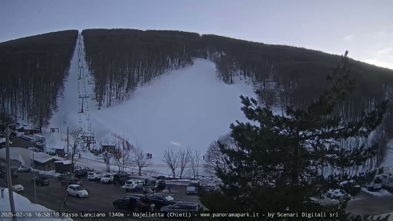 A ski slope with a chairlift and a parking lot full of cars is visible under a twilight sky.