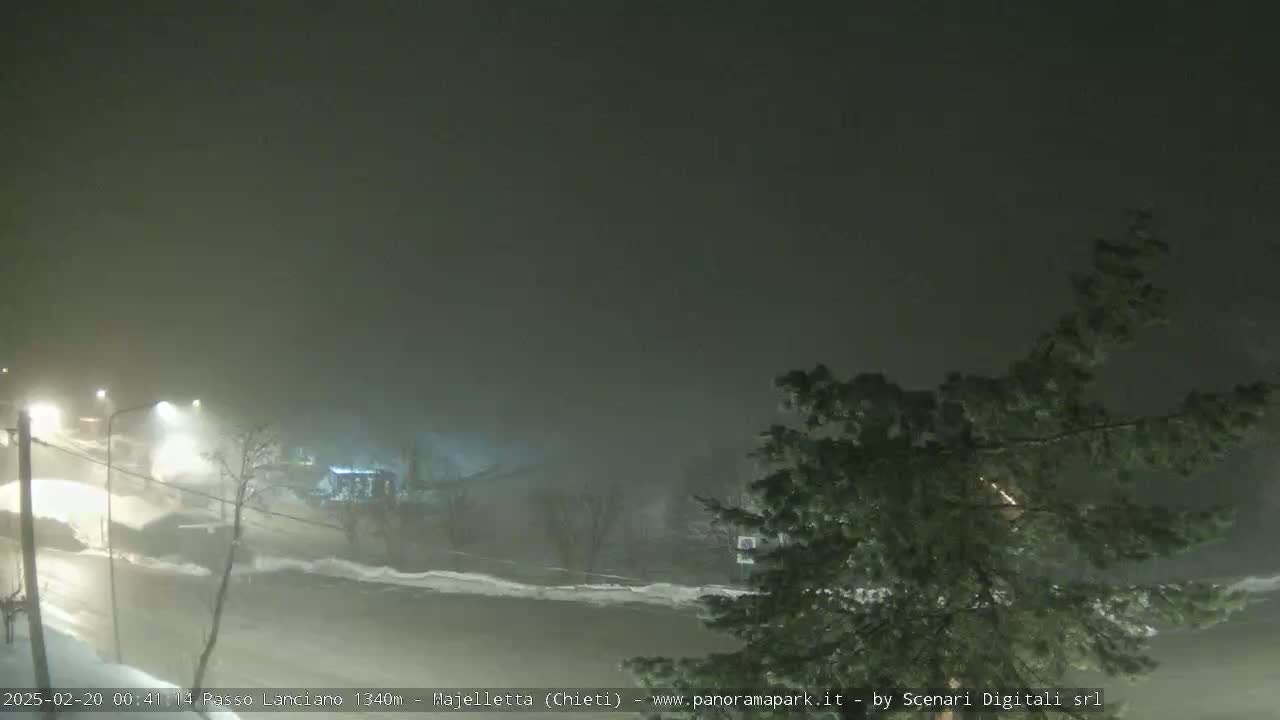 A snow-covered road scene is dimly lit at night under heavy snowfall.
