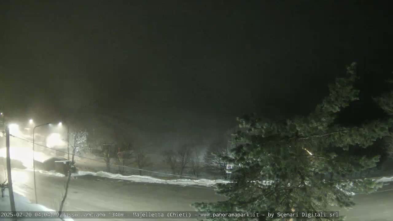 A nighttime scene of a snow-covered road with vehicles driving through heavy snow and fog.