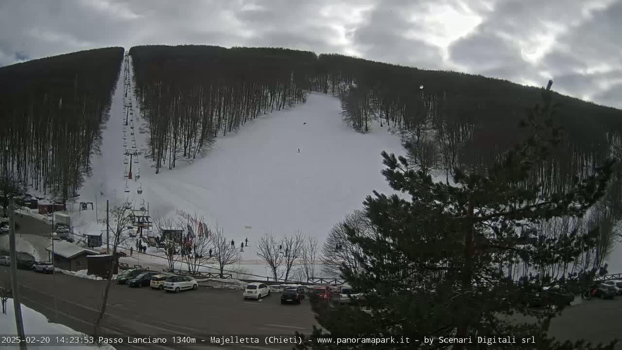A ski slope with a chairlift and a parking lot is visible under an overcast sky.
