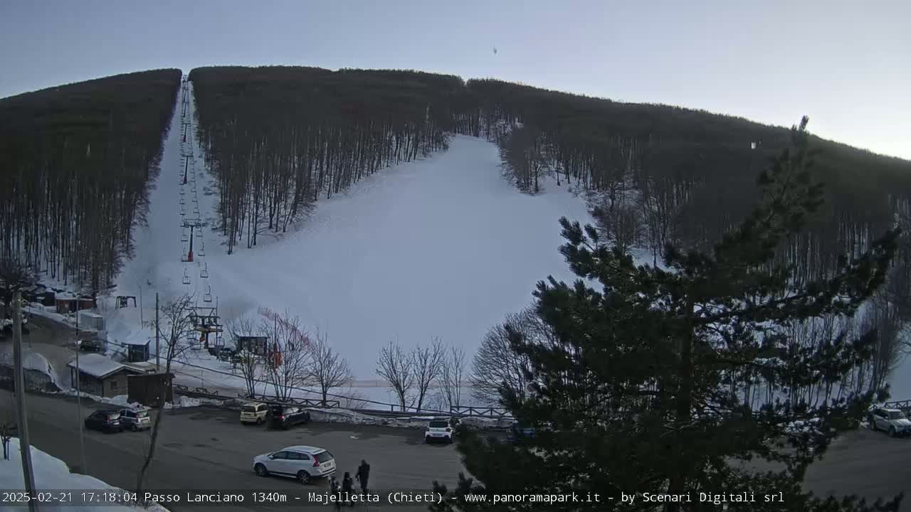 A ski slope with a chairlift visible, surrounded by snow-covered trees under a clear, twilight sky.
