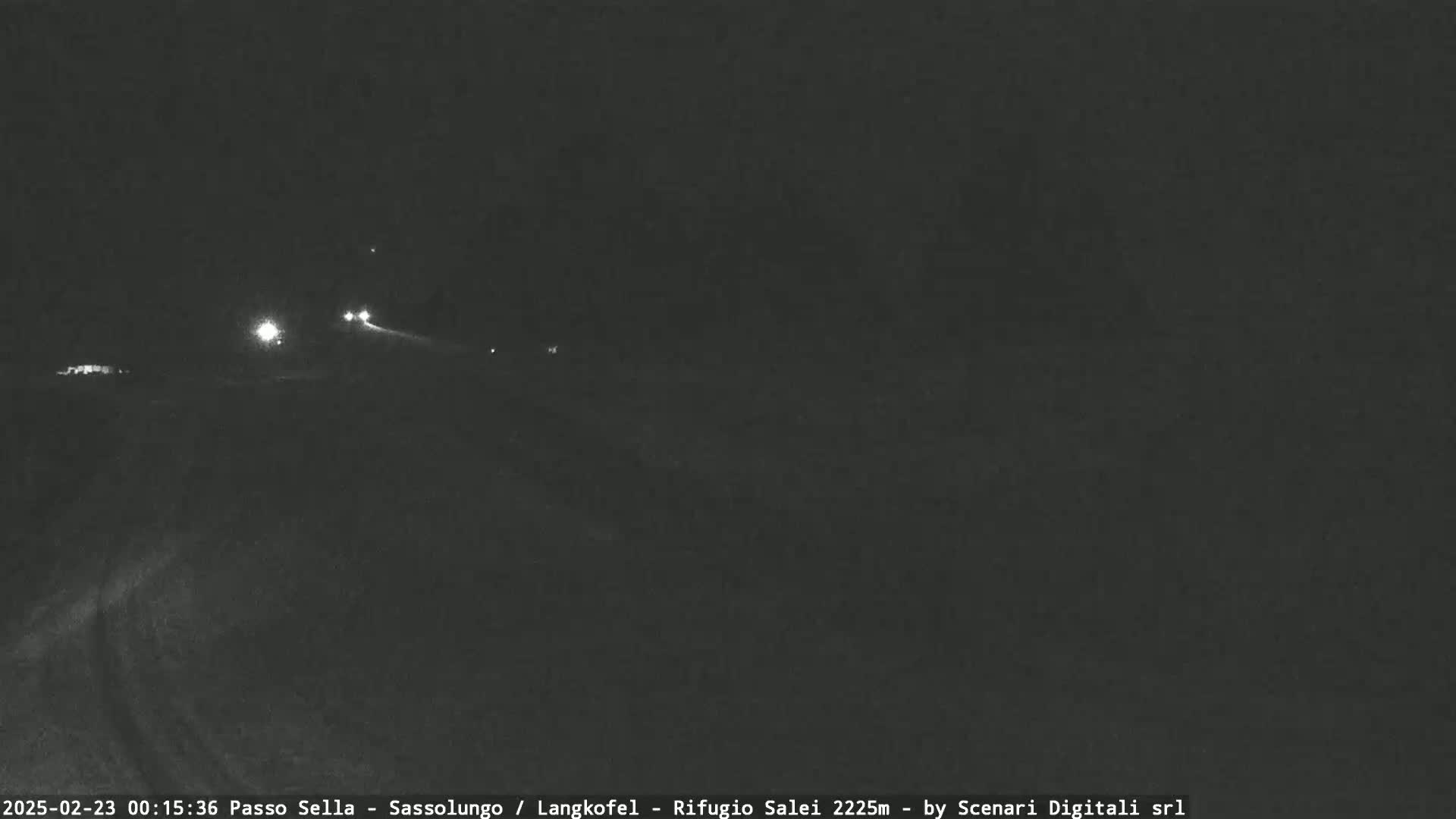 A nighttime, dark view of a road with a few distant headlights visible.