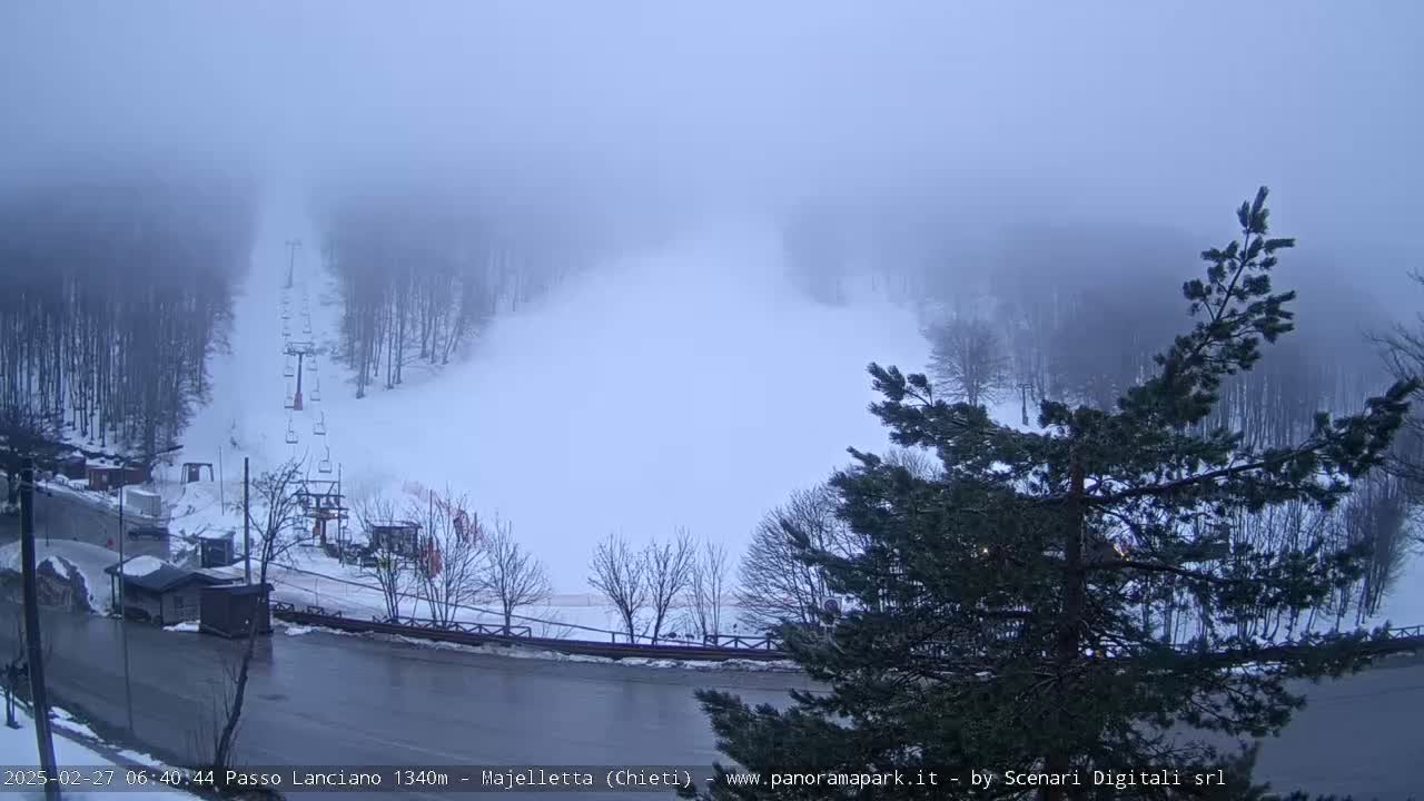 A snowy ski slope with a chairlift is shrouded in thick fog.