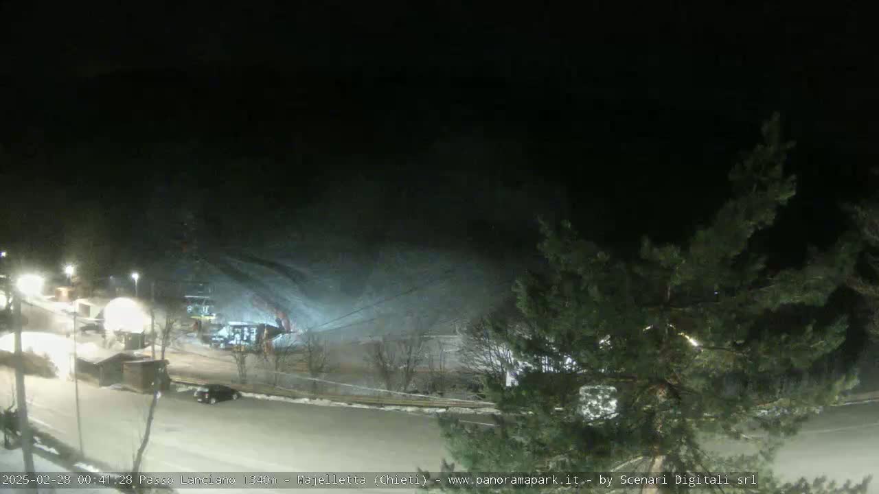 A nighttime, snow-covered parking lot and ski slope are visible under a dark sky.