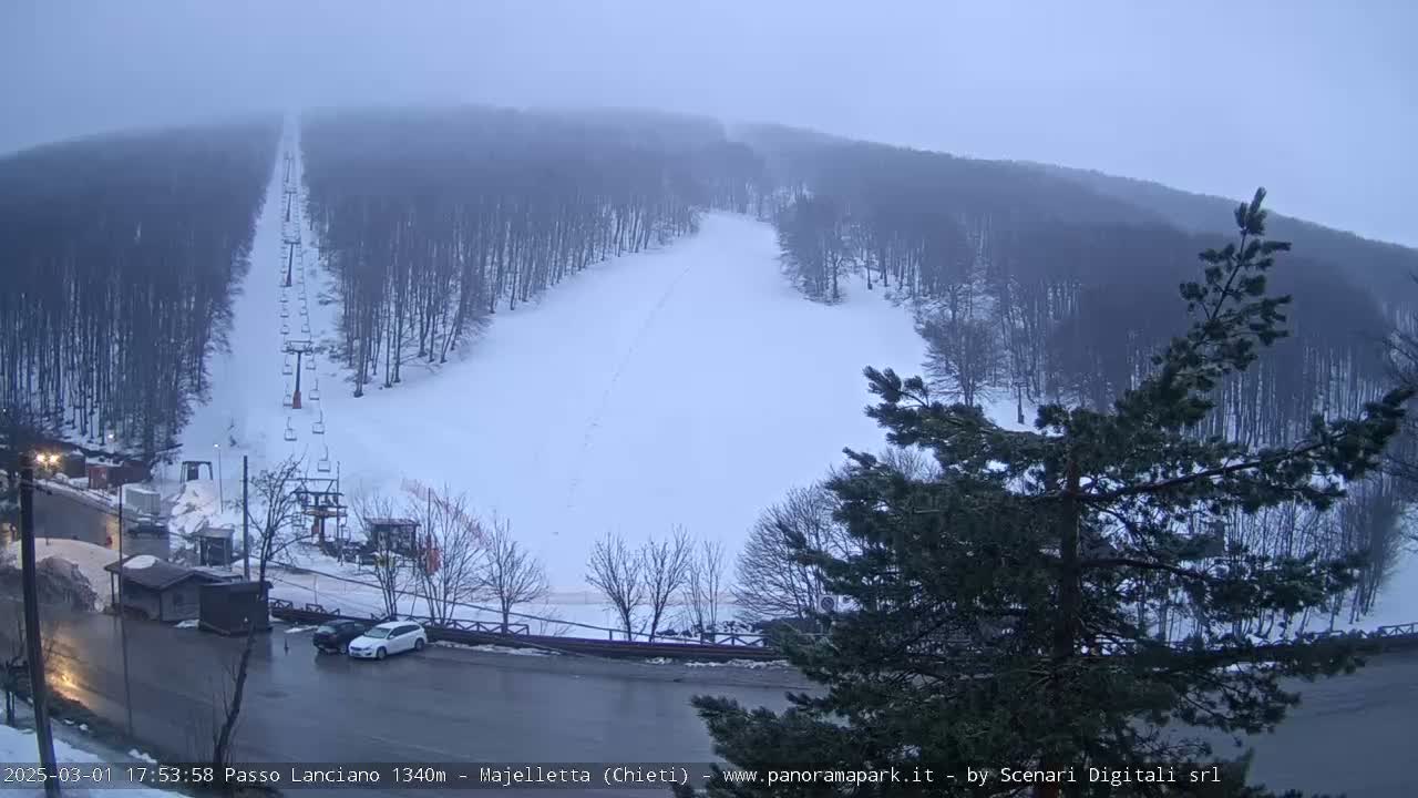 A snowy ski slope with a chairlift is visible through a hazy, overcast sky.