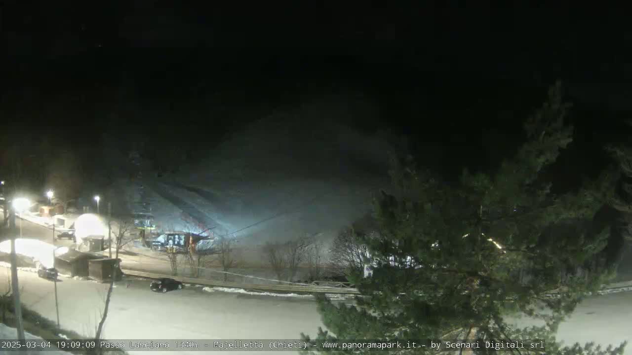 A nighttime, snow-covered ski slope is visible, with a parking lot and several small structures illuminated below.