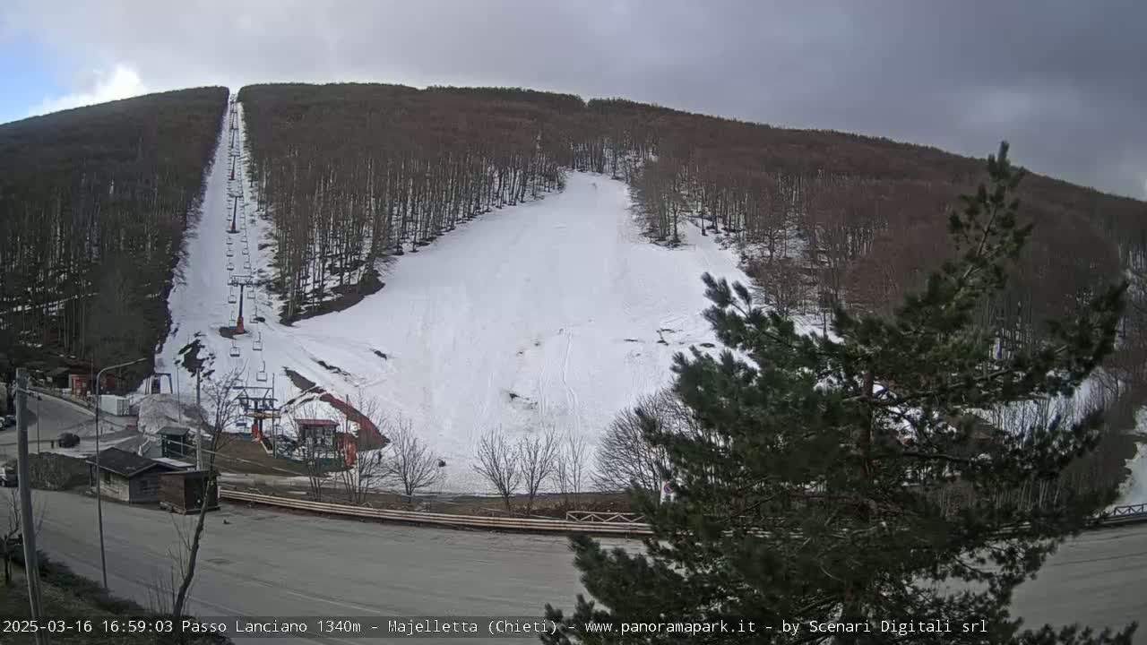 A snow-covered ski slope with a chairlift ascends a hillside of leafless trees under an overcast sky.