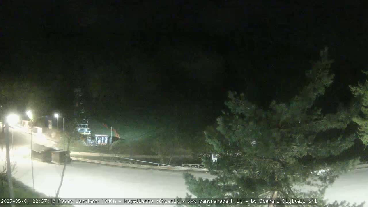 A nighttime, snow-covered parking lot and ski lift area are visible, partially obscured by trees.