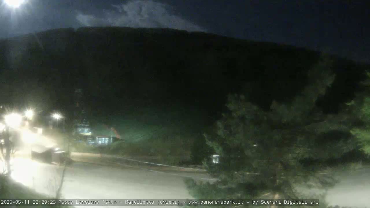 A nighttime view of a dark mountainside overlooking a sparsely lit road with a few vehicles.