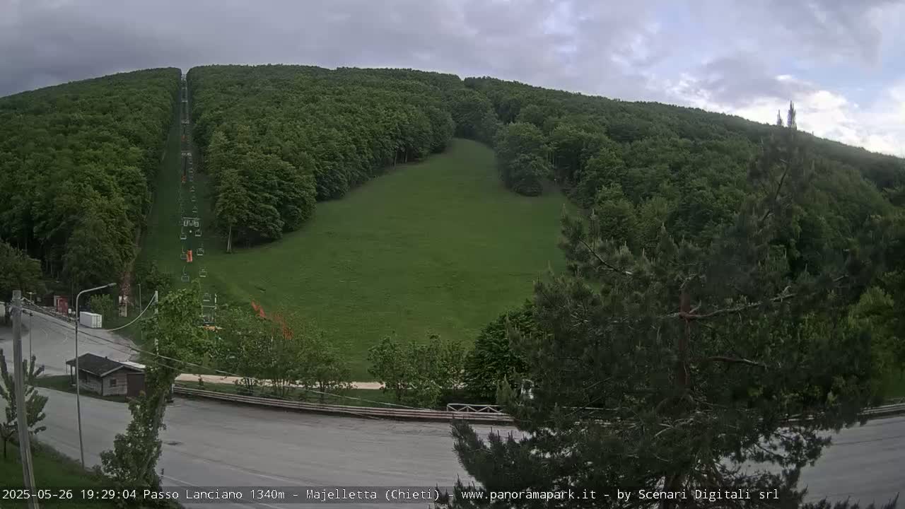A grassy hill with a chairlift and surrounding green forest is visible under an overcast sky.