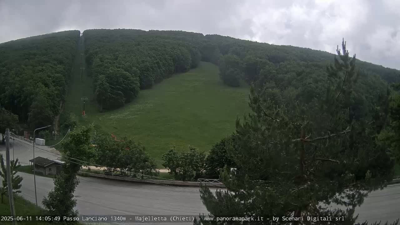 A grassy hillside with a ski lift running up its center is visible under an overcast sky.