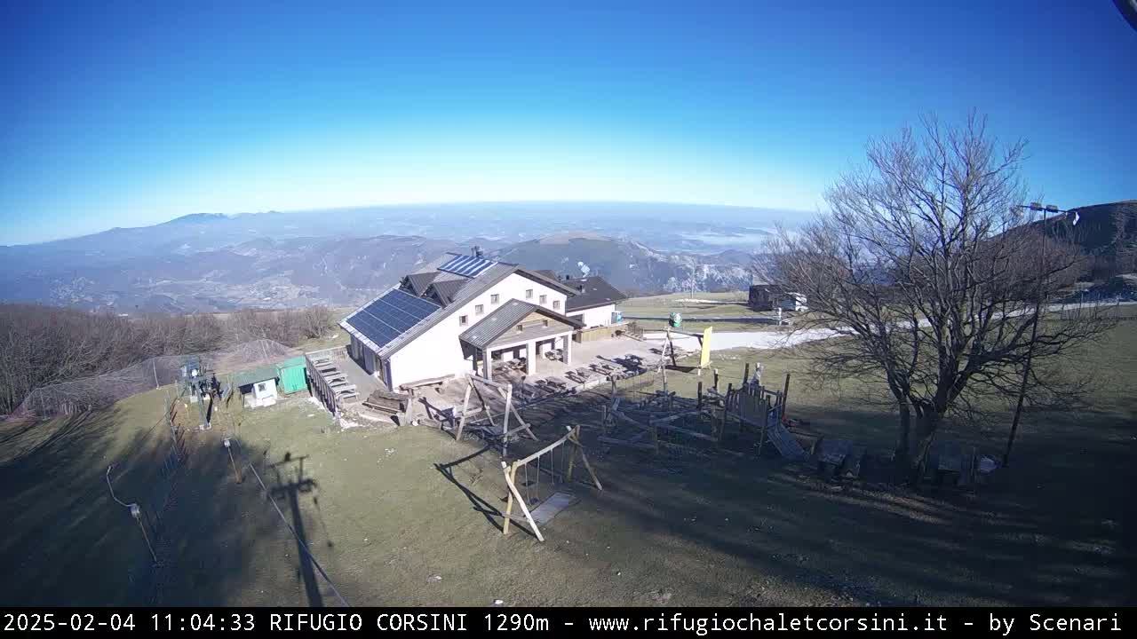 A mountaintop building with solar panels and a playground is visible under a clear blue sky, overlooking a vast, hazy valley.