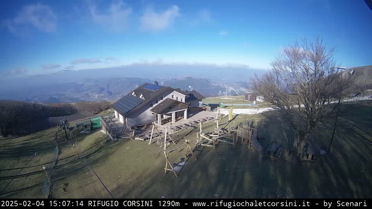 A mountaintop building with solar panels, a playground, and a ski lift, under a clear blue sky with some haze in the distance.