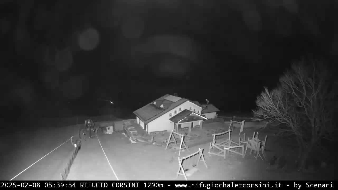 A nighttime, black-and-white view shows a building with a playground next to a road under a dark, possibly cloudy sky.