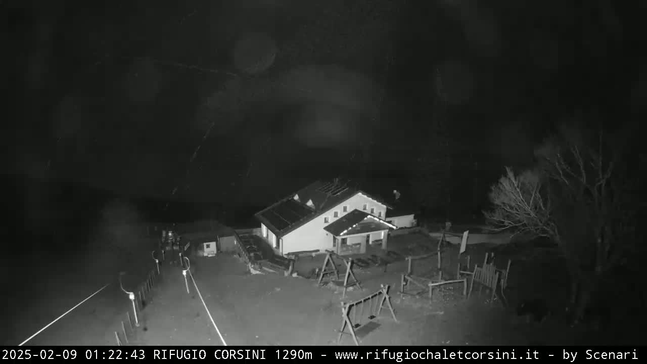 A nighttime, low-light image shows a building with a playground next to a road under a dark, possibly stormy sky.
