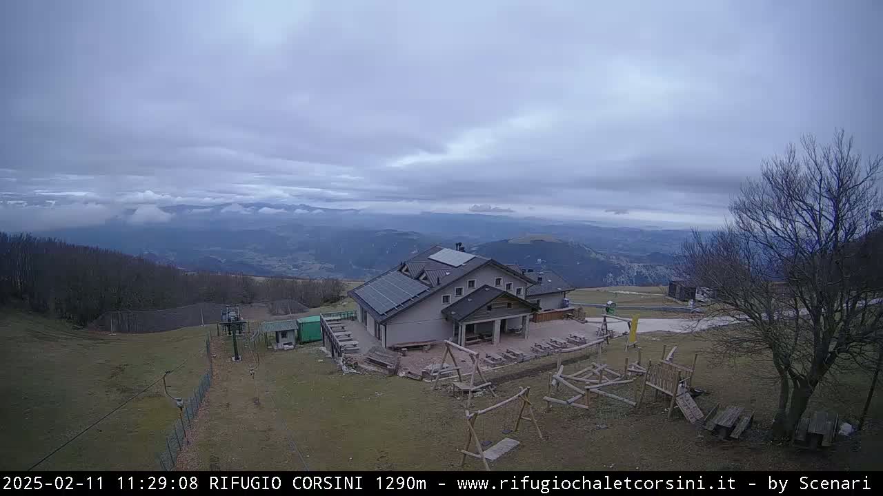 A mountaintop building with solar panels sits below an overcast sky, overlooking a valley shrouded in low clouds.