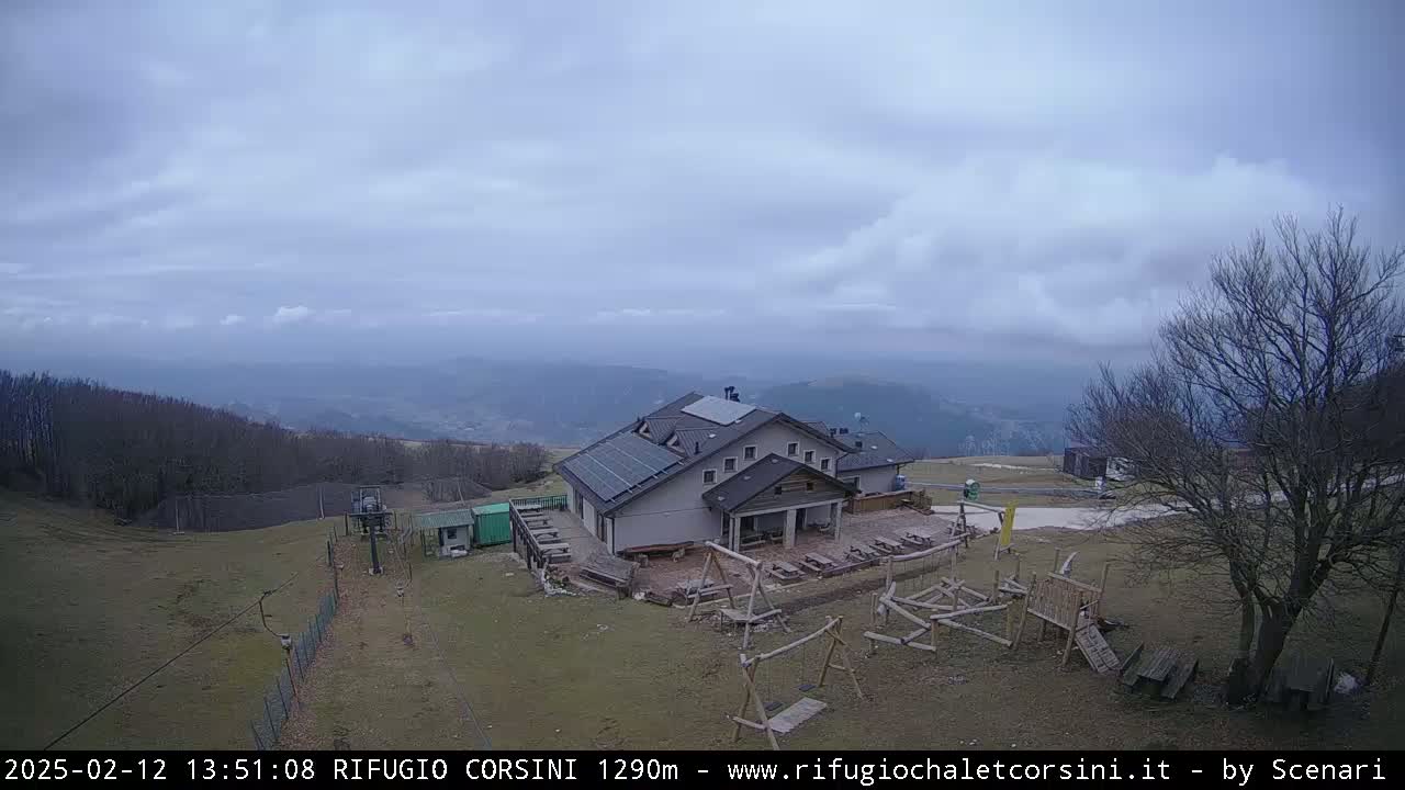 A mountaintop building with solar panels, playground equipment, and a view of distant hills under a cloudy sky.