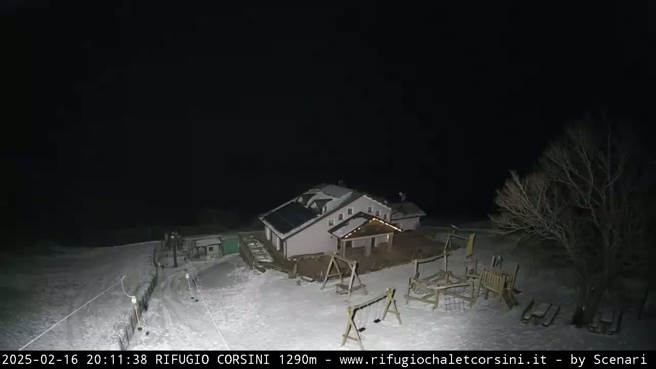 A snow-covered building with a playground and a few trees is visible at night under a dark sky.