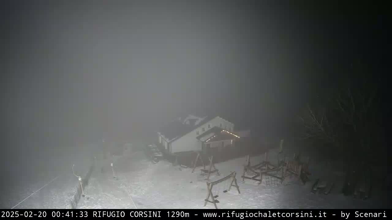 A building with playground equipment is visible through heavy fog at night, with snow on the ground.