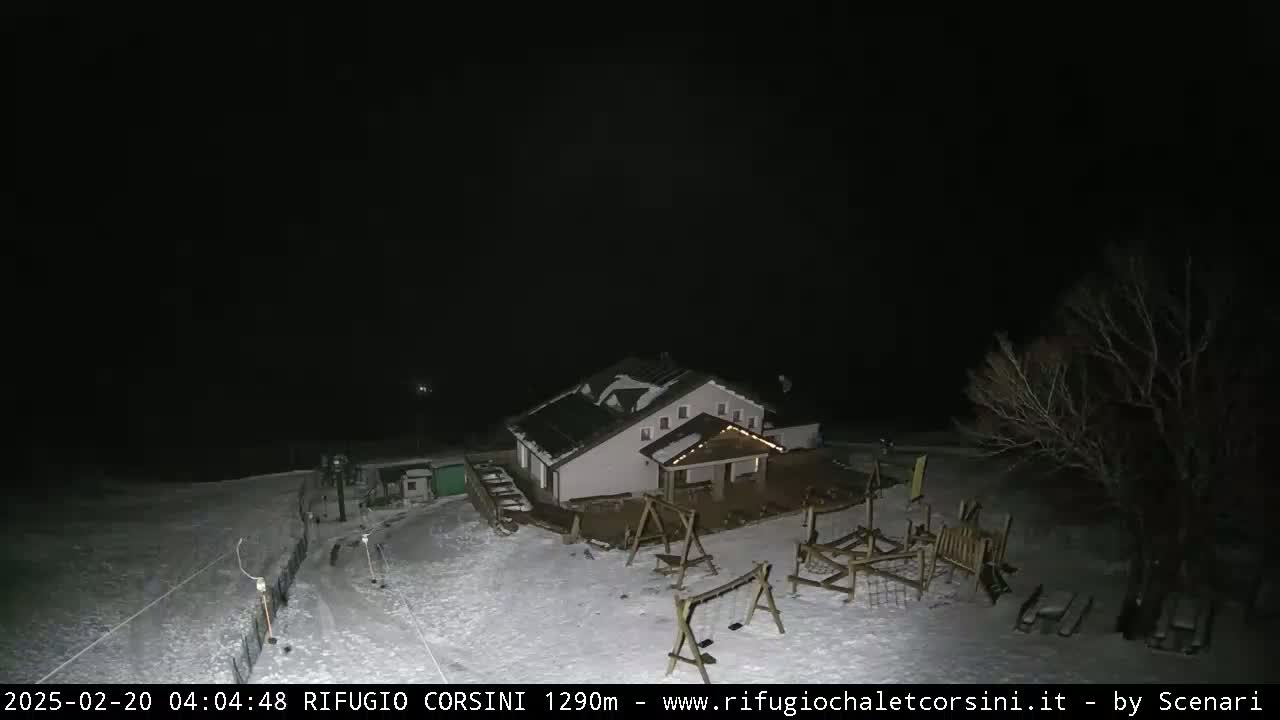 A snow-covered playground and building are illuminated at night under a dark sky.