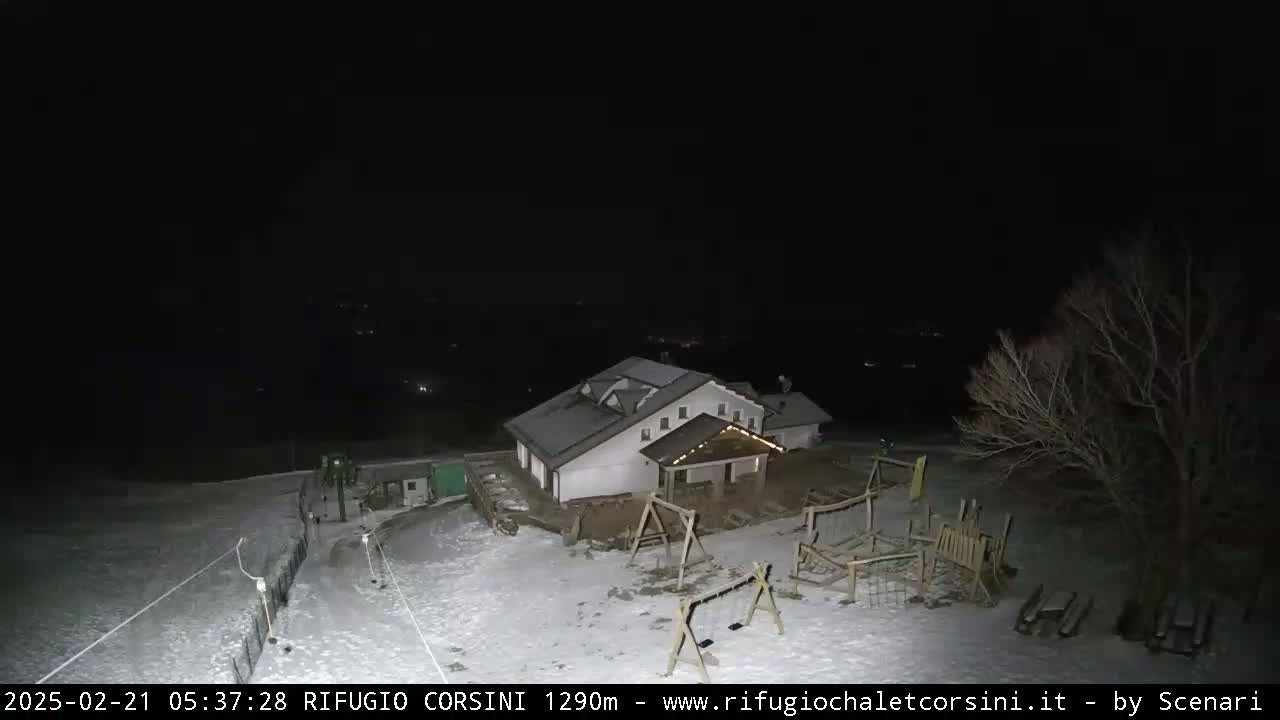 A snow-covered playground and building are illuminated at night.