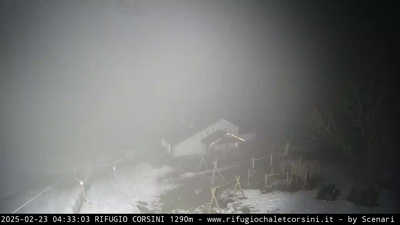 A dimly lit building and some outdoor structures are barely visible through heavy fog at night.