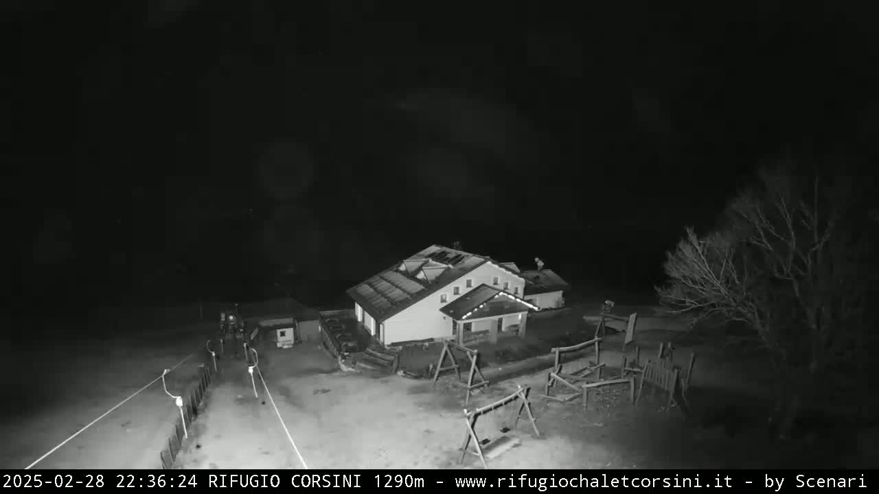 A nighttime, high-angle, black-and-white view shows a building with a playground and some bare trees under a dark, clear sky.