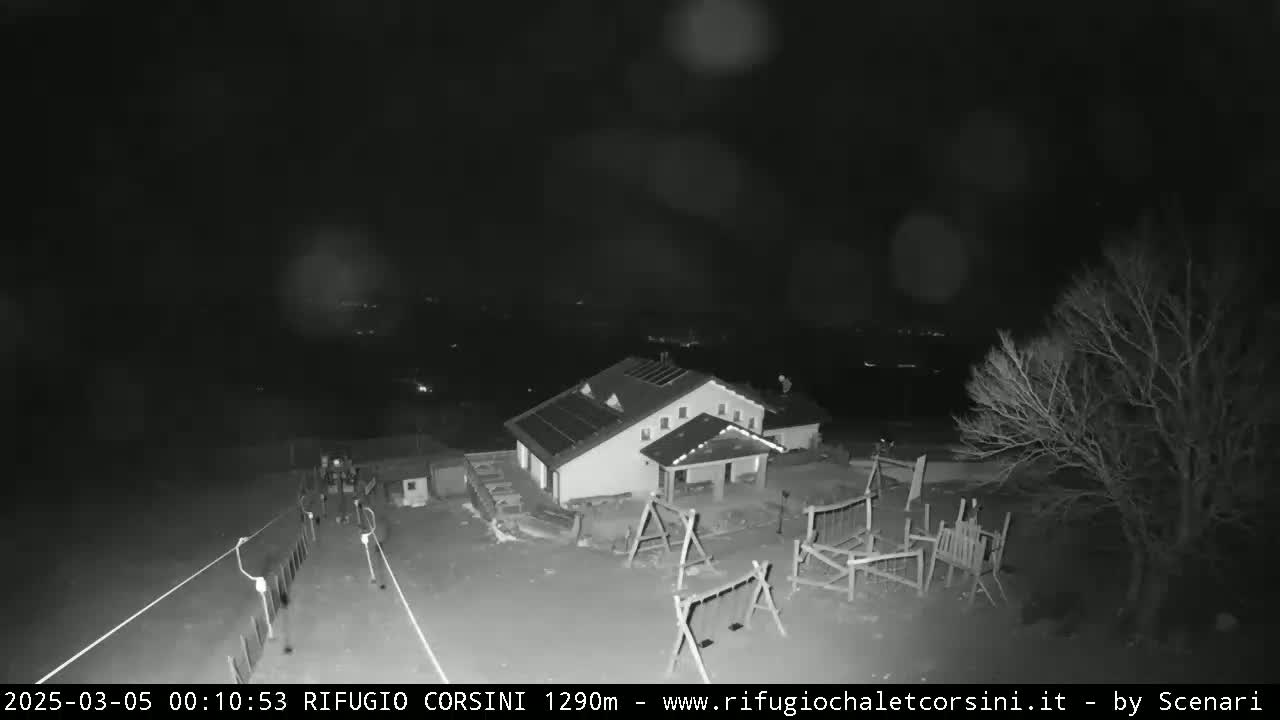A nighttime, low-light view shows a building with a playground and a few bare trees under a dark, possibly snowy sky.