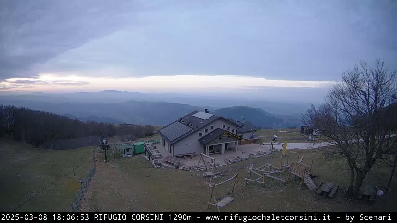 A mountaintop building with a playground sits overlooking a hazy valley under a mostly cloudy sky.