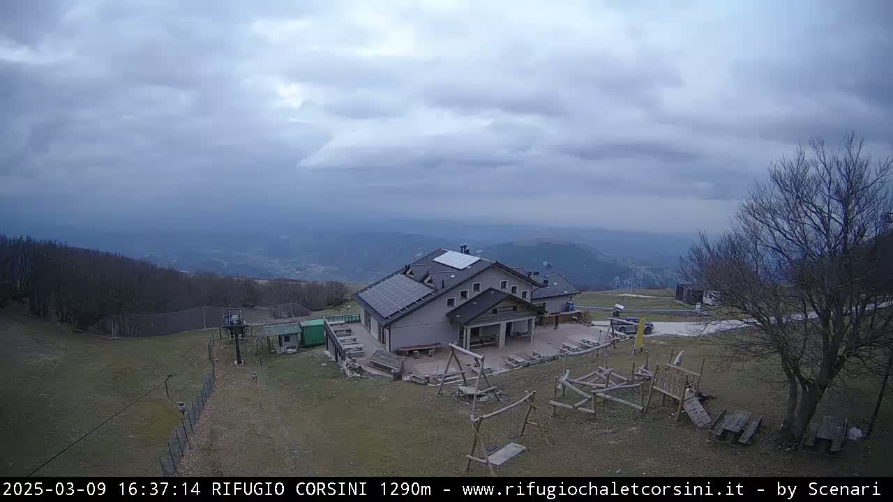 A mountaintop building with solar panels and a playground sits under an overcast sky overlooking a valley.