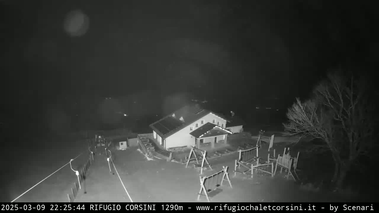 A nighttime, low-light view shows a building with a playground next to it, and a few bare trees in the background.