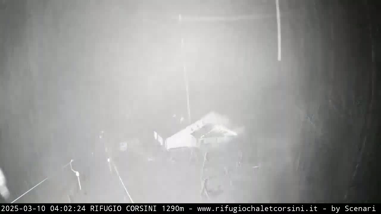 A blurry, low-visibility outdoor scene shows a building and indistinct figures in heavy snow or fog.