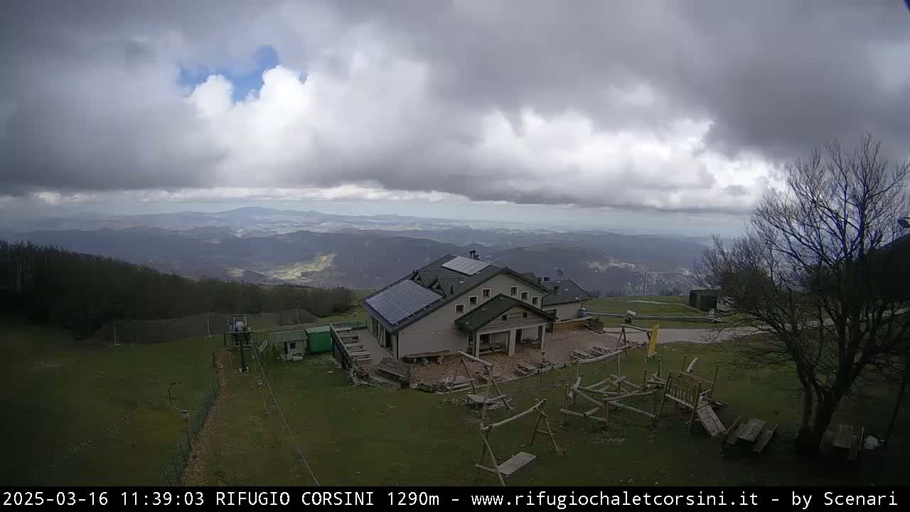 A mountaintop building with solar panels sits overlooking a vast valley under a cloudy sky.