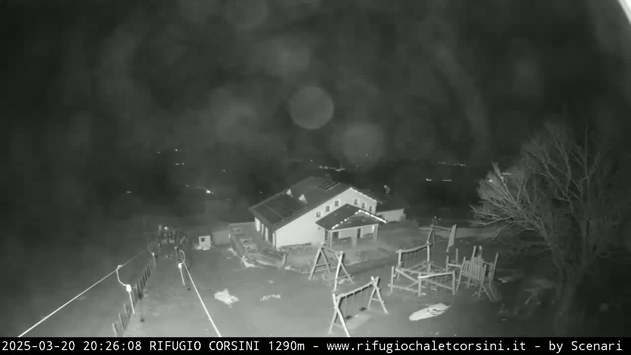 A nighttime, blurry black-and-white image shows a building with a playground next to it, under a cloudy sky.