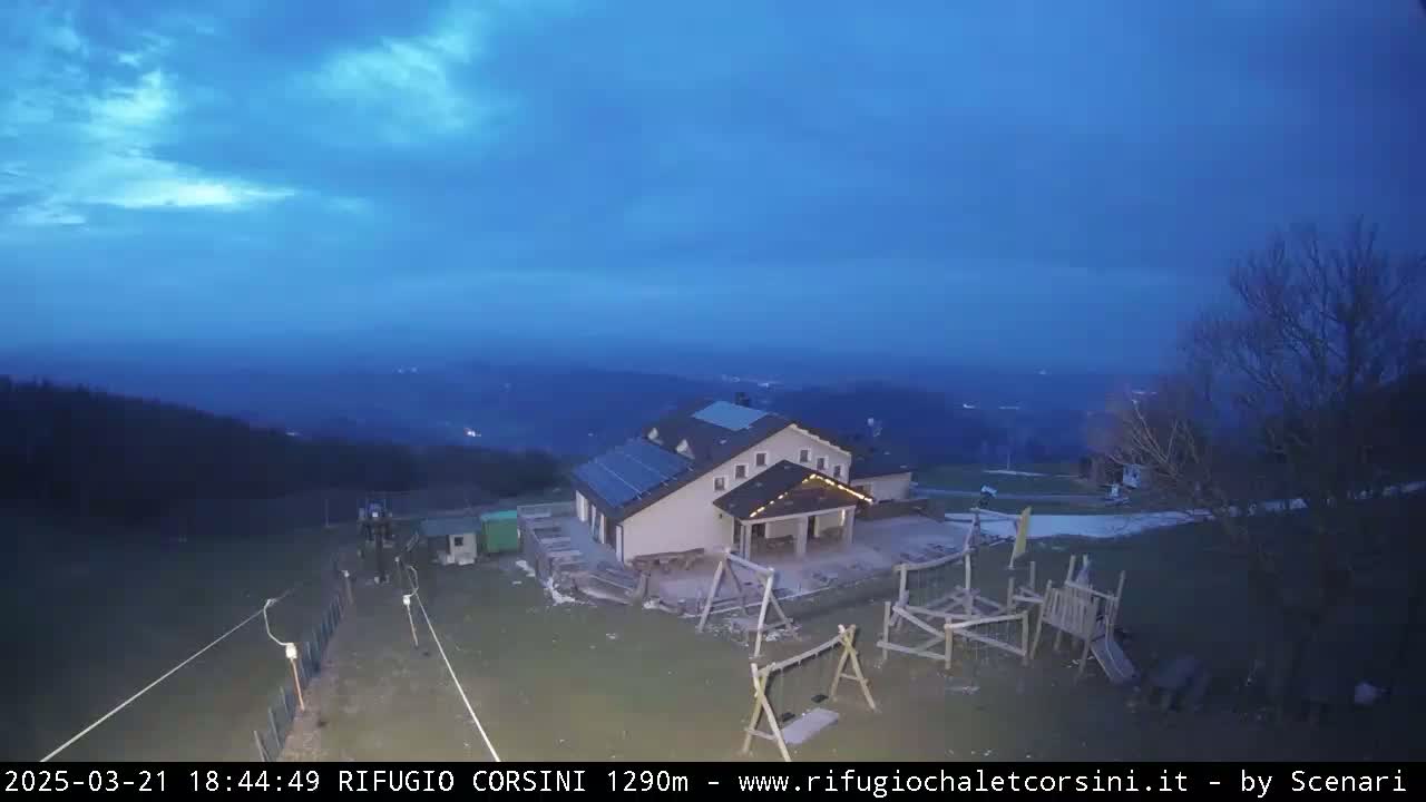 A building with solar panels and a playground sits on a hilltop at dusk under a mostly clear, dark blue sky.