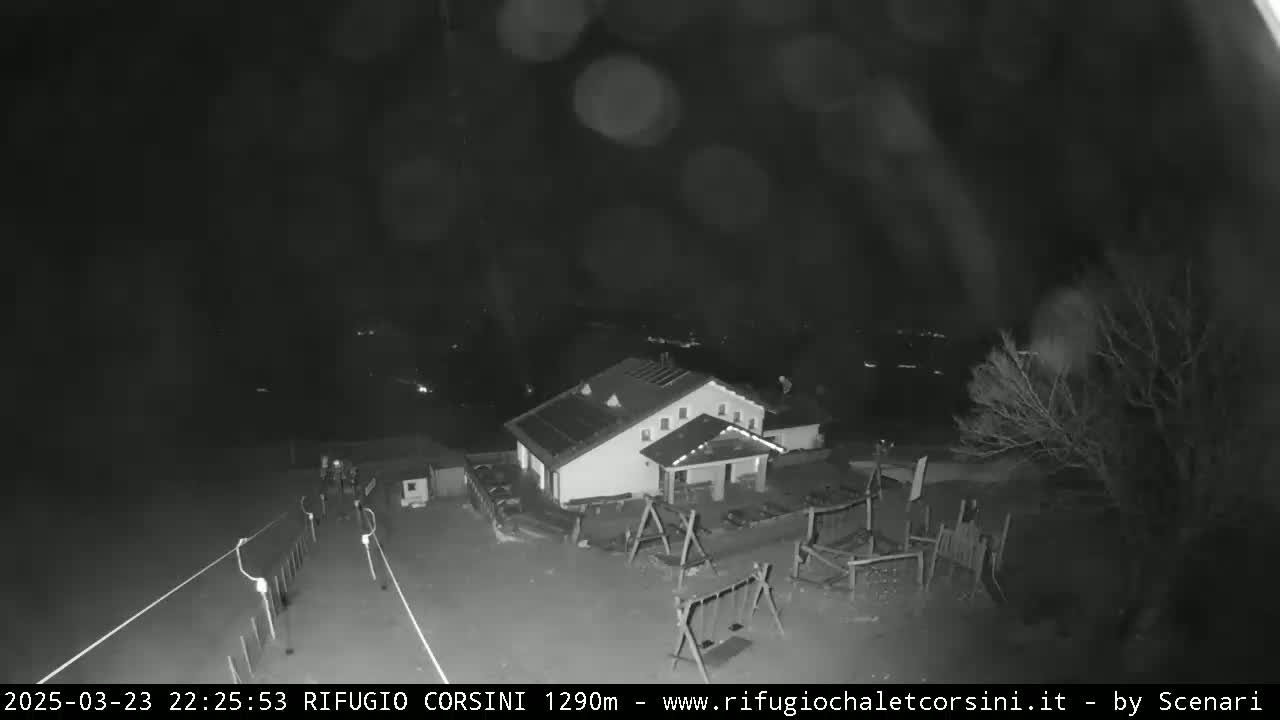 A nighttime, snowy scene shows a building with a playground in front of it, and a road leading away.