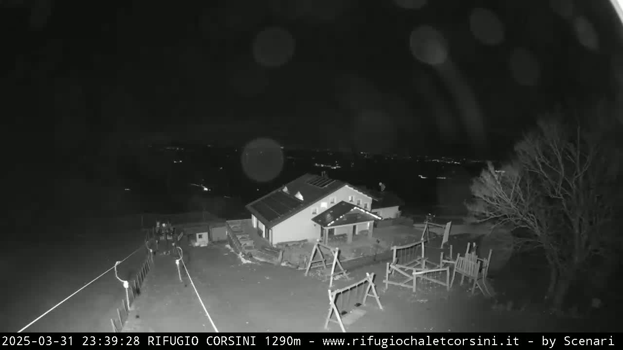 A nighttime, black-and-white view shows a building with a playground and distant lights, under a dark, possibly cloudy sky.