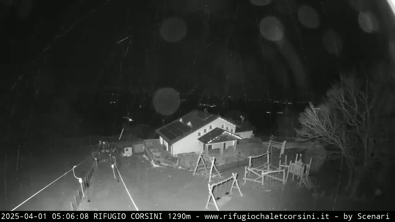 A nighttime, snowy scene shows a building with a playground, illuminated by faint lights, against a dark background with distant city lights.