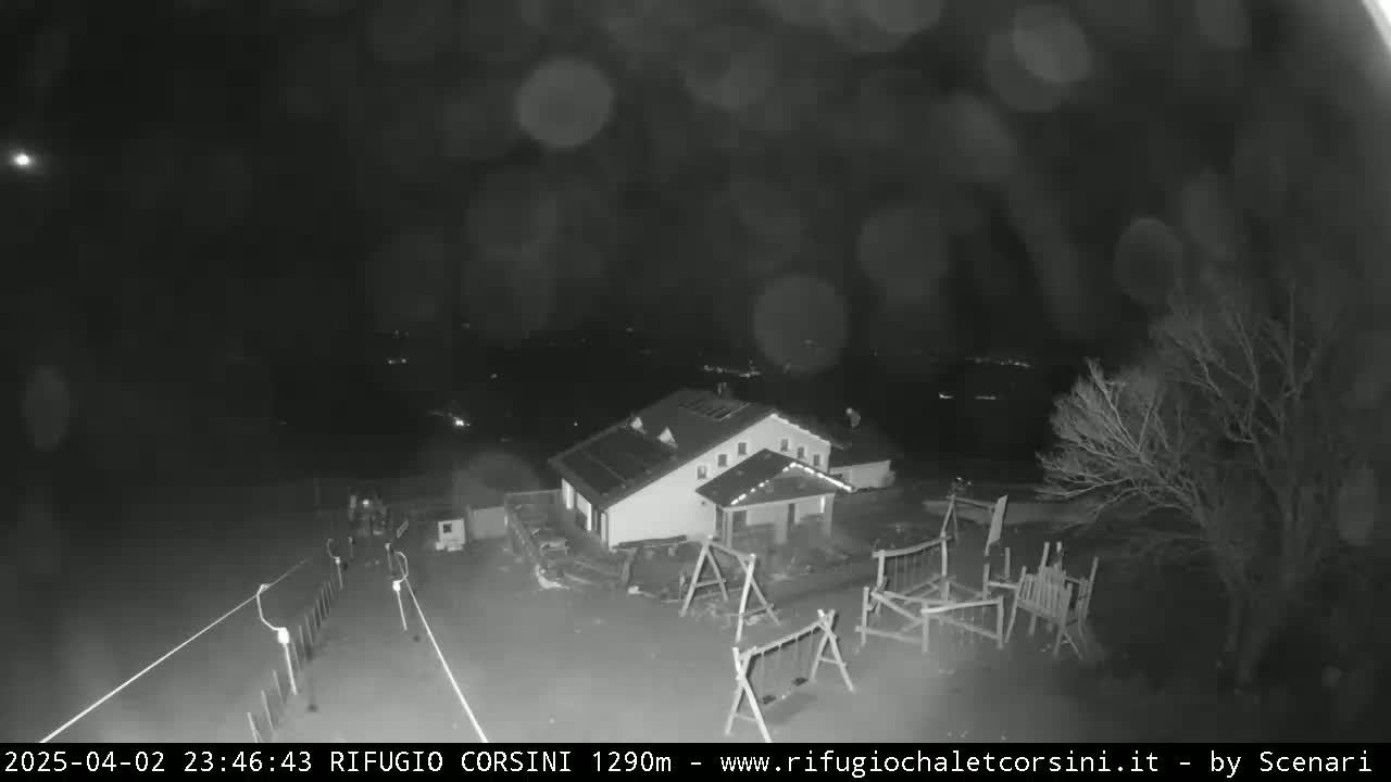 A nighttime, blurry black-and-white image shows a building with solar panels, a playground, and some trees under a dark, possibly snowy or hazy sky.