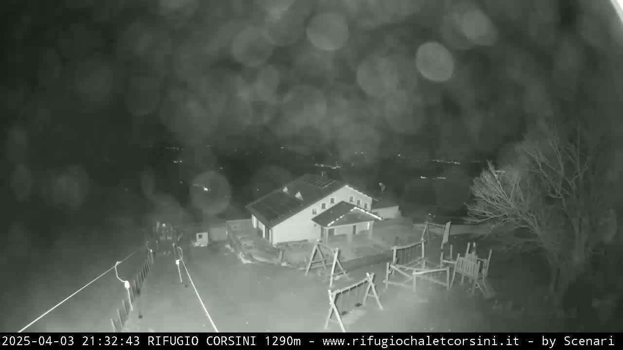 A nighttime, blurry, rain-streaked view of a building with a playground, situated on a hill overlooking a valley.