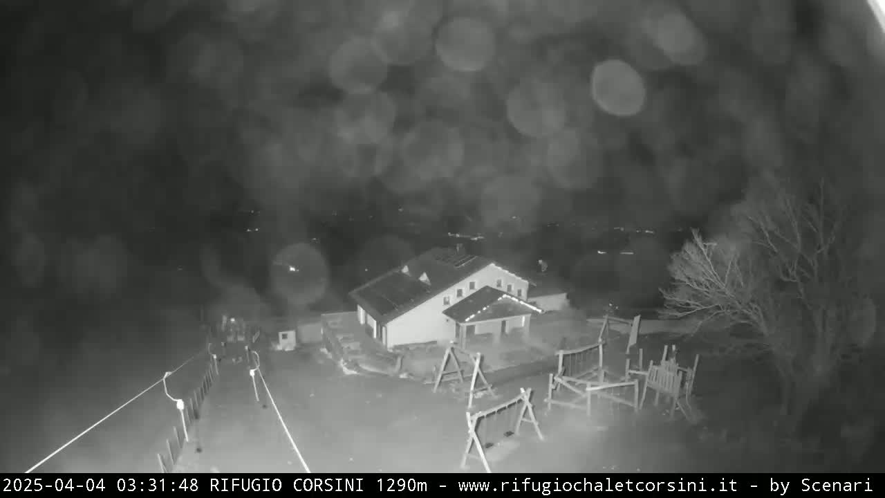 A nighttime, rainy view shows a building with a playground and surrounding trees.
