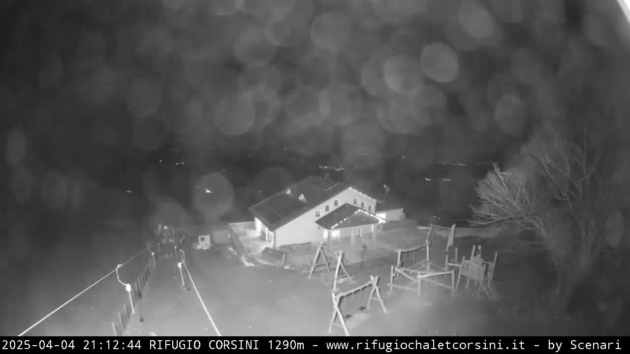 A nighttime, blurry, low-light view of a building with a playground, surrounded by bare trees under a cloudy sky.