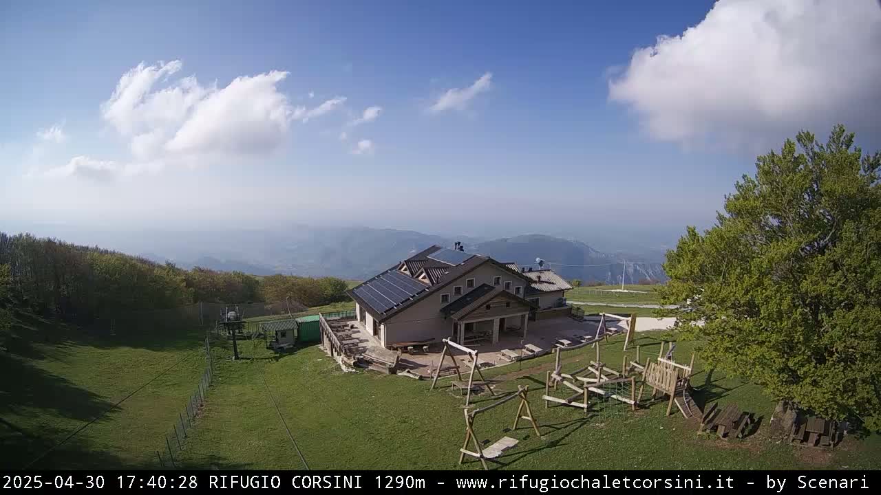 A mountaintop building with solar panels and a playground is visible under a partly cloudy sky, overlooking a hazy valley.