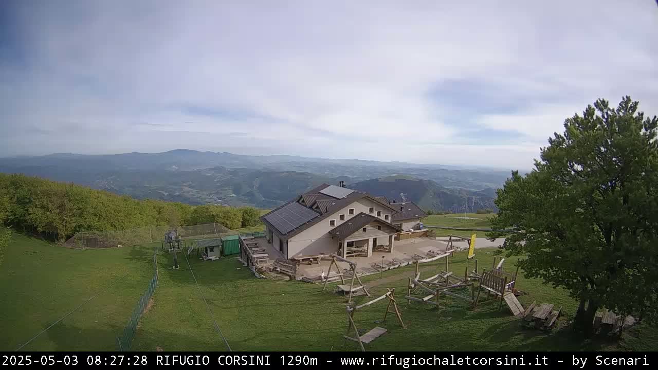 A mountaintop building with solar panels, a playground, and a view of rolling hills under a partly cloudy sky.