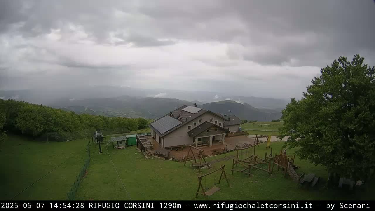 A mountain lodge with solar panels is situated on a grassy area with a playground, under an overcast sky.